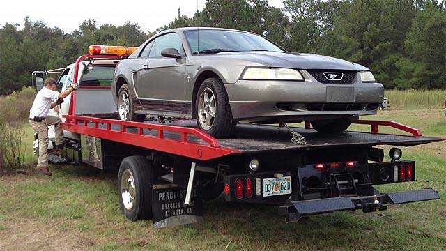 A silver car is being towed by a red tow truck.